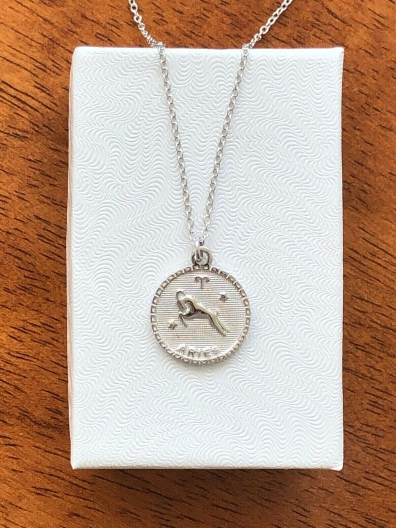May include: A silver necklace with a circular pendant featuring the zodiac symbol for Aries. The pendant has a detailed design of a ram with the word "Aries" inscribed below.