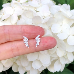 May include: A pair of silver earrings with a delicate, curved design. Each earring is adorned with small, sparkling cubic zirconia stones.