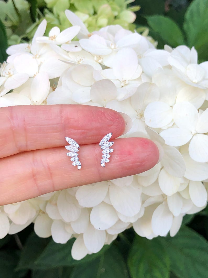 May include: A pair of silver earrings with a delicate, curved design. Each earring is adorned with small, sparkling cubic zirconia stones.
