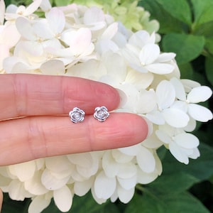 May include: A pair of silver rose-shaped earrings with a small clear stone in the center of each rose.