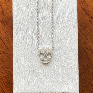 Puede incluir: Un collar de cadena de plata con un peque&ntilde;o colgante de calavera incrustado con circonita c&uacute;bica.