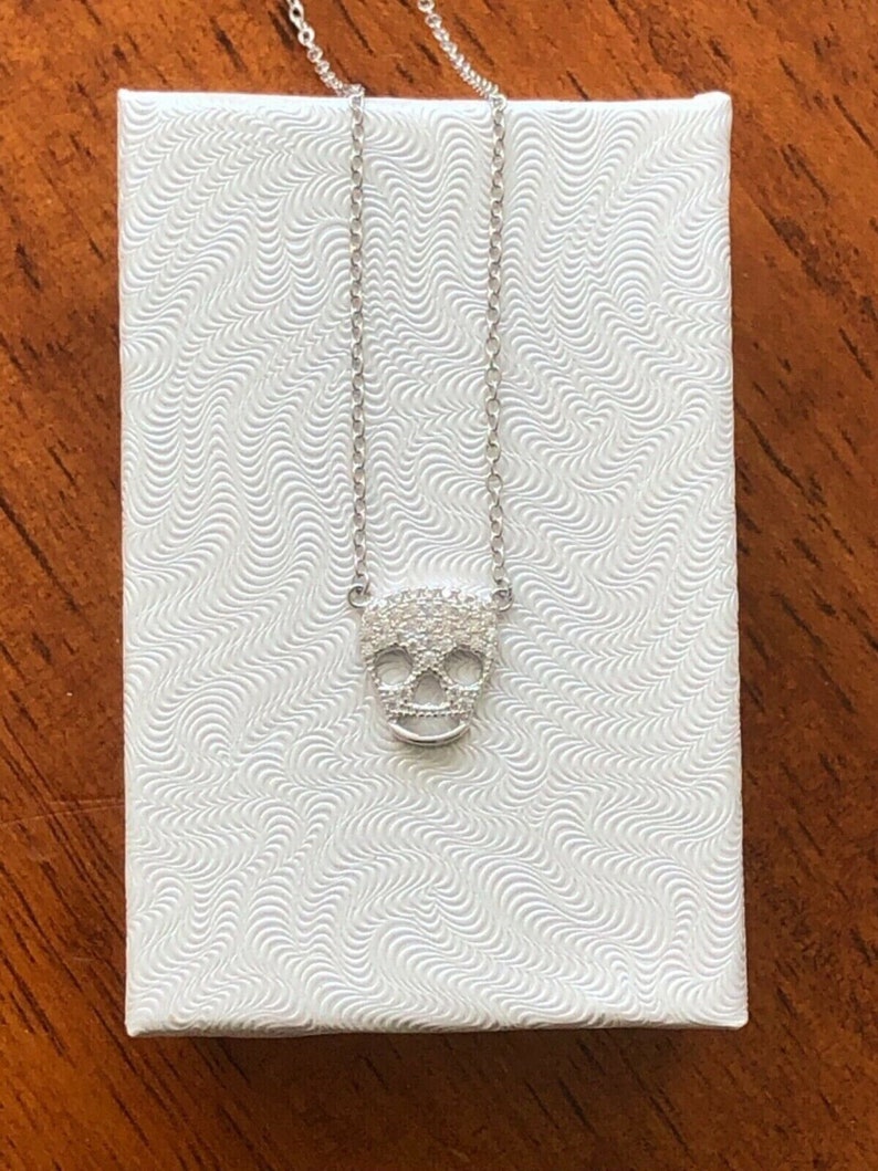 Puede incluir: Un collar de cadena de plata con un peque&ntilde;o colgante de calavera incrustado con circonita c&uacute;bica.