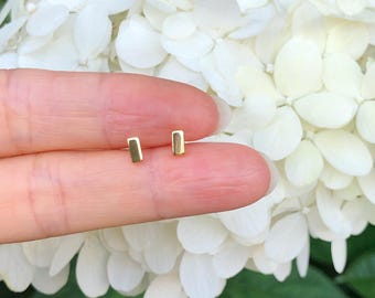 May include: A pair of gold bar stud earrings. The earrings are small and simple, and they are perfect for everyday wear.