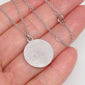 May include: A silver chain necklace with a round silver pendant. The pendant has a textured surface.