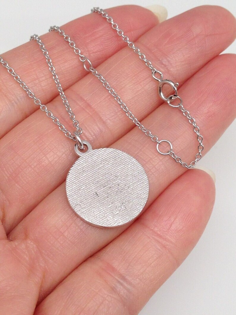 May include: A silver chain necklace with a round silver pendant. The pendant has a textured surface.