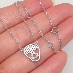 Puede incluir: Un collar de cadena de plata con un colgante de calavera de plata. La calavera est&aacute; hecha de peque&ntilde;as piedras redondas que est&aacute;n engastadas en un patr&oacute;n delicado.