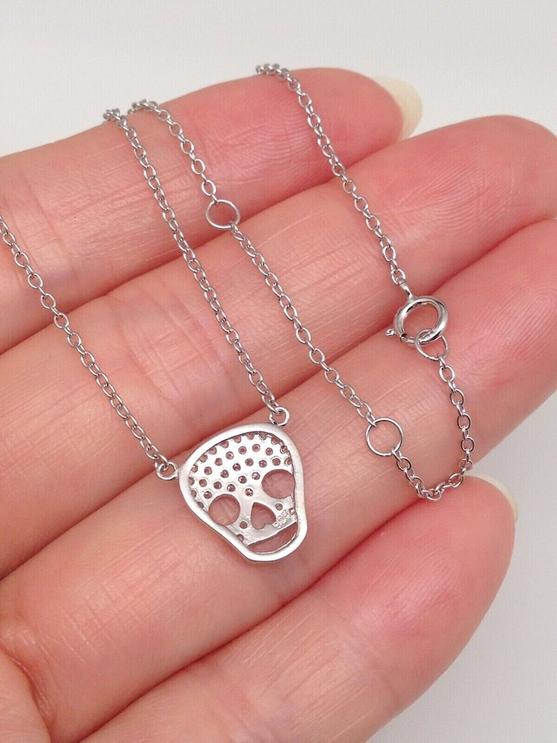 Puede incluir: Un collar de cadena de plata con un colgante de calavera de plata. La calavera est&aacute; hecha de peque&ntilde;as piedras redondas que est&aacute;n engastadas en un patr&oacute;n delicado.
