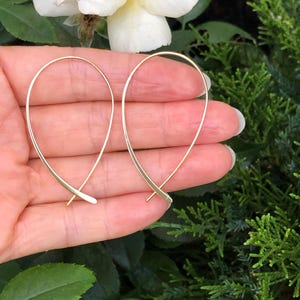 May include: A pair of gold-toned hoop earrings with a simple, minimalist design. The earrings are made of thin wire and have a delicate, crossed shape.