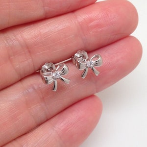 May include: A pair of silver bow earrings with a small clear rhinestone in the center of each bow.