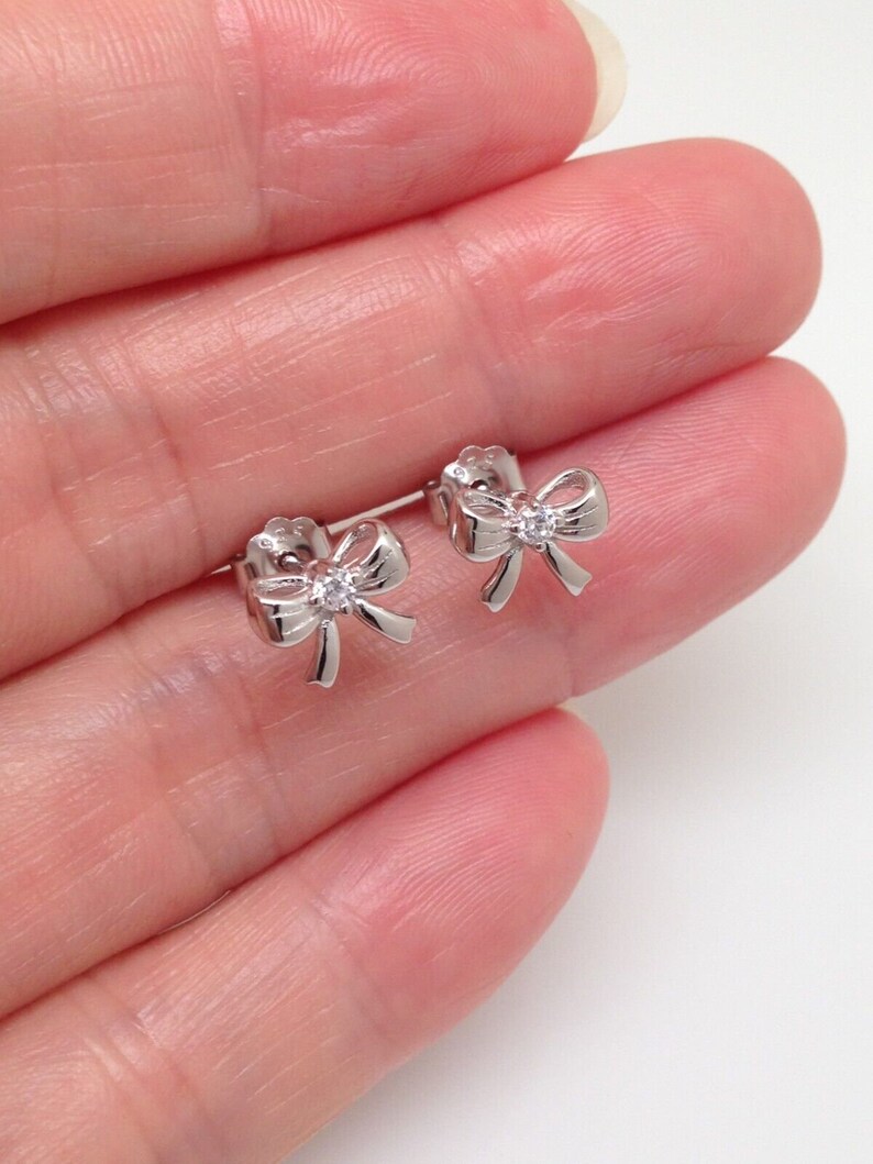 May include: A pair of silver bow earrings with a small clear rhinestone in the center of each bow.