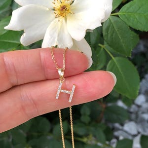 May include: A gold chain necklace with a small pendant in the shape of the letter H. The pendant is encrusted with small, clear cubic zirconia stones.