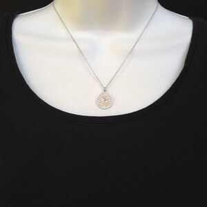 May include: A silver necklace with a round pendant featuring a zodiac symbol. The pendant has a textured edge and a delicate chain.