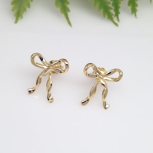 Puede incluir: Un par de pendientes de color dorado en forma de lazo. Los lazos est&aacute;n hechos de alambre retorcido.