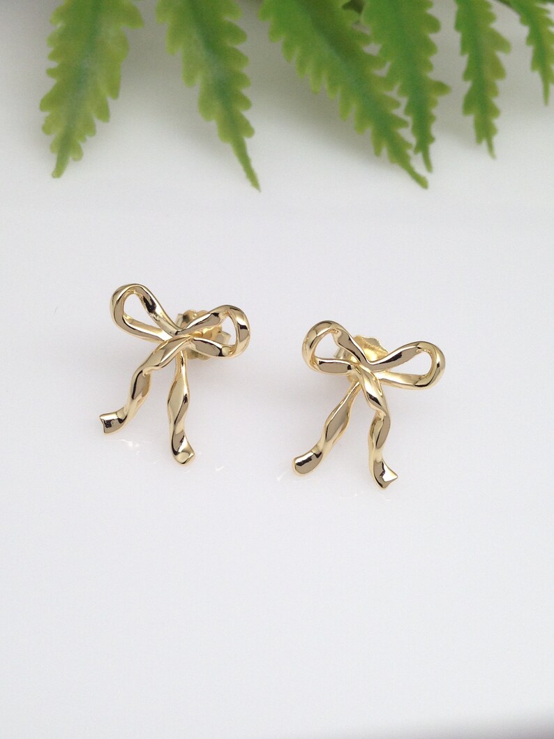 Puede incluir: Un par de pendientes de color dorado en forma de lazo. Los lazos est&aacute;n hechos de alambre retorcido.