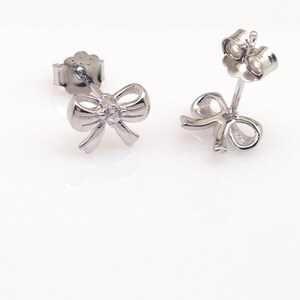 May include: A pair of silver bow earrings with a small clear rhinestone in the center of each bow.