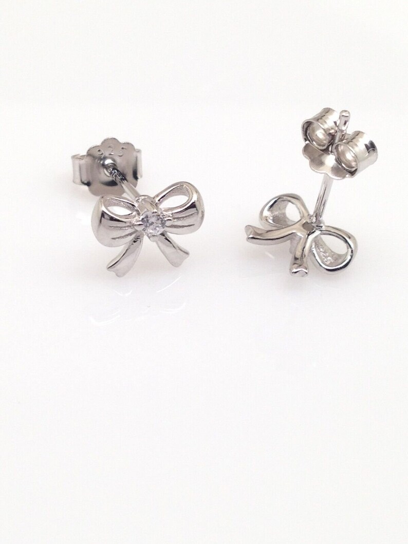 May include: A pair of silver bow earrings with a small clear rhinestone in the center of each bow.