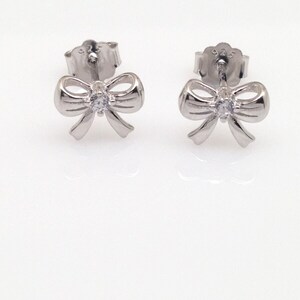 May include: A pair of silver bow earrings with a small clear rhinestone in the center of each bow.