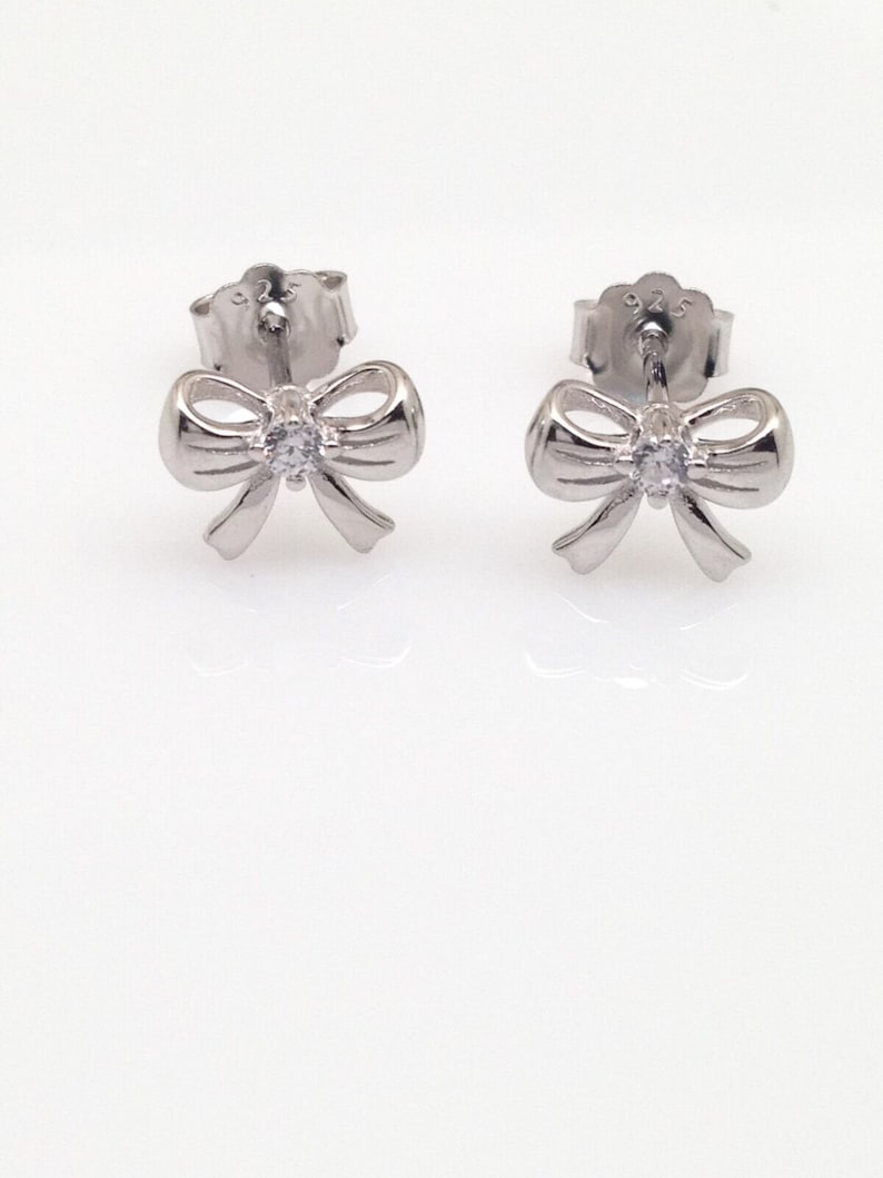 May include: A pair of silver bow earrings with a small clear rhinestone in the center of each bow.