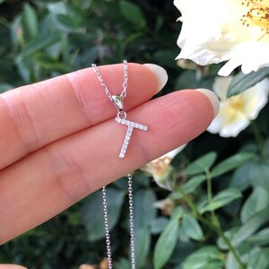 May include: A silver chain necklace with a letter T pendant encrusted with small clear stones.