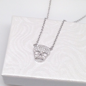 Puede incluir: Un collar de cadena de plata con un peque&ntilde;o colgante de calavera brillante. El colgante est&aacute; hecho de plata y tiene un engaste de pav&eacute; de piedras de circonita c&uacute;bica transparentes.