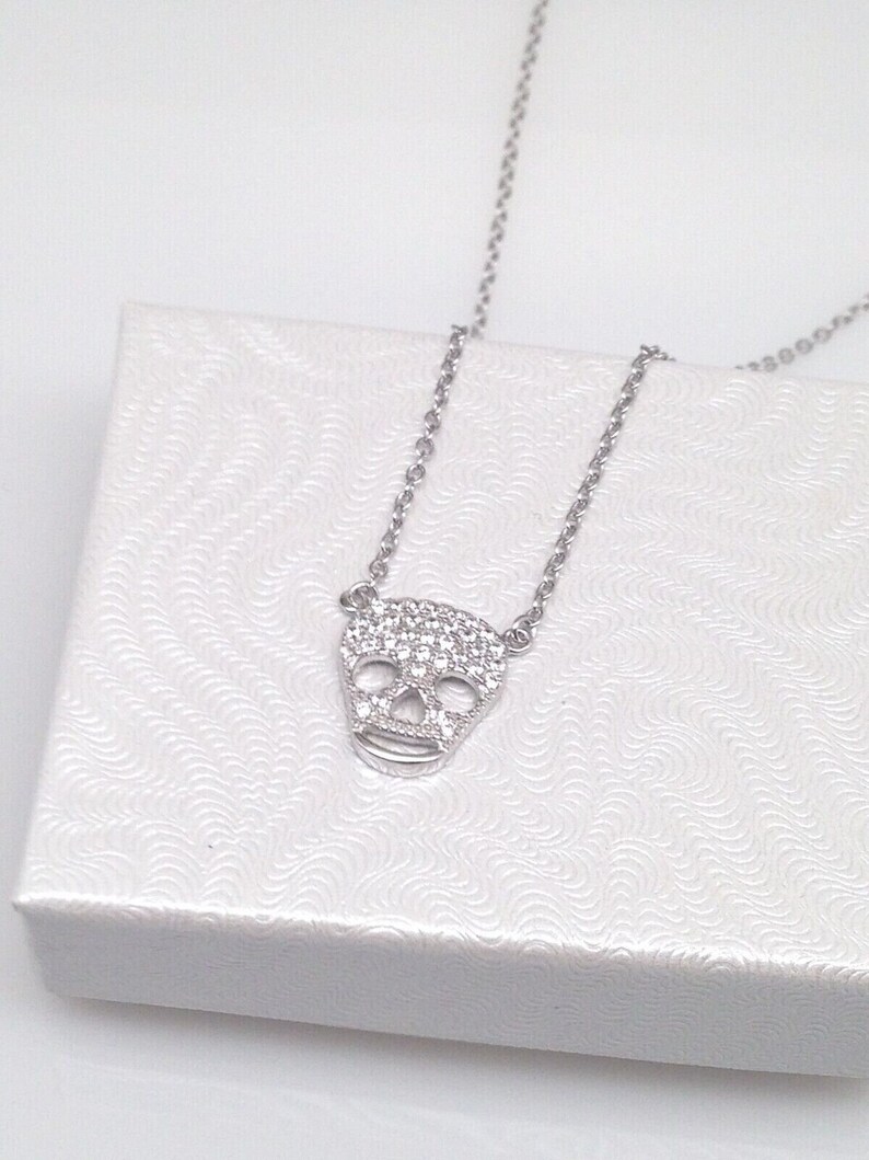 Puede incluir: Un collar de cadena de plata con un peque&ntilde;o colgante de calavera brillante. El colgante est&aacute; hecho de plata y tiene un engaste de pav&eacute; de piedras de circonita c&uacute;bica transparentes.