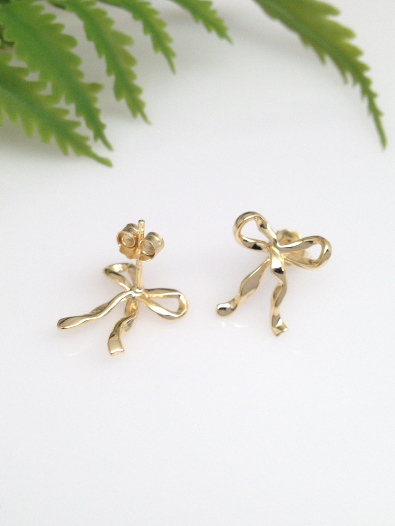 Puede incluir: Un par de pendientes de color dorado en forma de lazo. Los pendientes est&aacute;n hechos de metal retorcido y tienen un dise&ntilde;o simple y elegante.