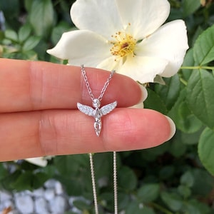 Puede incluir: Un collar de plata con un peque&ntilde;o colgante de &aacute;ngel adornado con piedras de circonita c&uacute;bica transparentes. El &aacute;ngel tiene las alas extendidas y un dise&ntilde;o delicado.