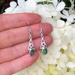 May include: Silver Celtic knot earrings with green oval-shaped gemstones. The earrings are dangling and have a Celtic knot design.