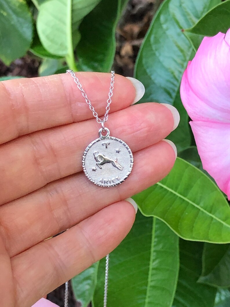 May include: Silver necklace with a round pendant featuring the zodiac symbol for Aries. The pendant has a detailed design of a ram with the word "Aries" inscribed below.