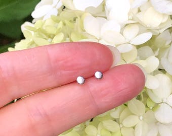 May include: A pair of small, silver stud earrings. The earrings are round and have a smooth, polished finish.