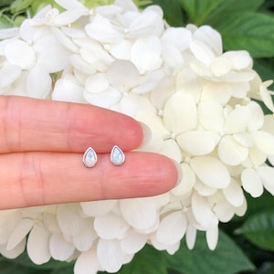 May include: A pair of silver teardrop-shaped earrings with white opal stones.