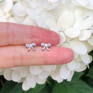 May include: A pair of silver bow-shaped stud earrings.