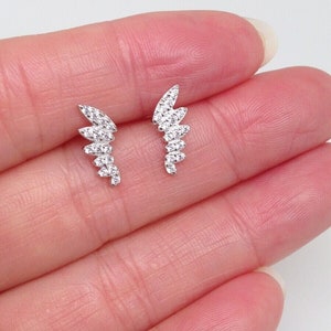 May include: A pair of silver earrings with a delicate, curved design. Each earring features a row of small, clear cubic zirconia stones.