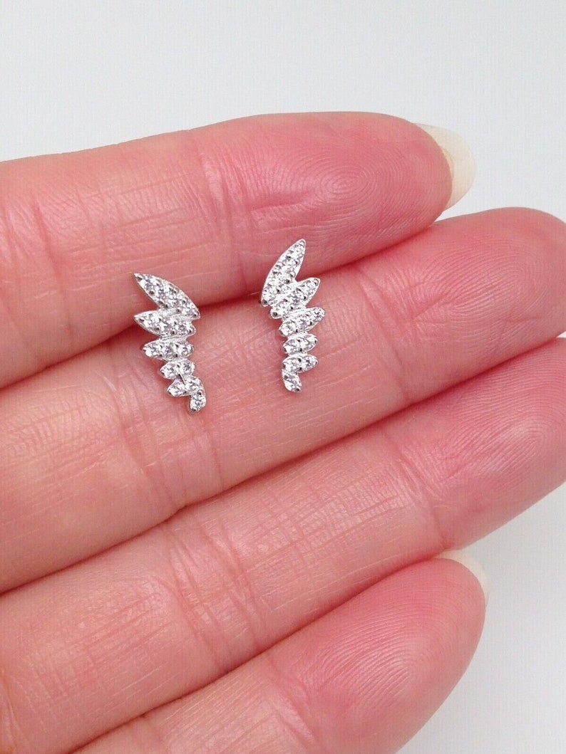 May include: A pair of silver earrings with a delicate, curved design. Each earring features a row of small, clear cubic zirconia stones.