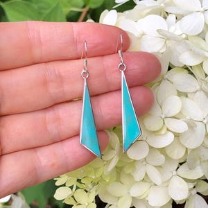 May include: A pair of silver dangle earrings with turquoise stones in a geometric shape.
