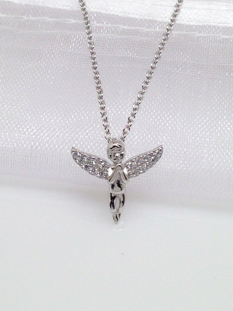 Puede incluir: Un collar de plata con un peque&ntilde;o colgante de &aacute;ngel detallado. El &aacute;ngel lleva un vestido y tiene alas con peque&ntilde;as piedras transparentes.