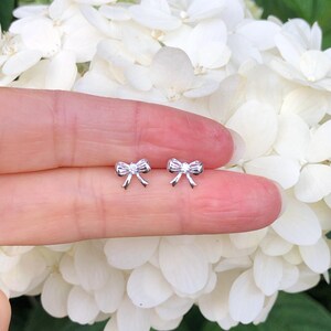 May include: A pair of silver bow earrings with a small clear stone in the center of each bow.