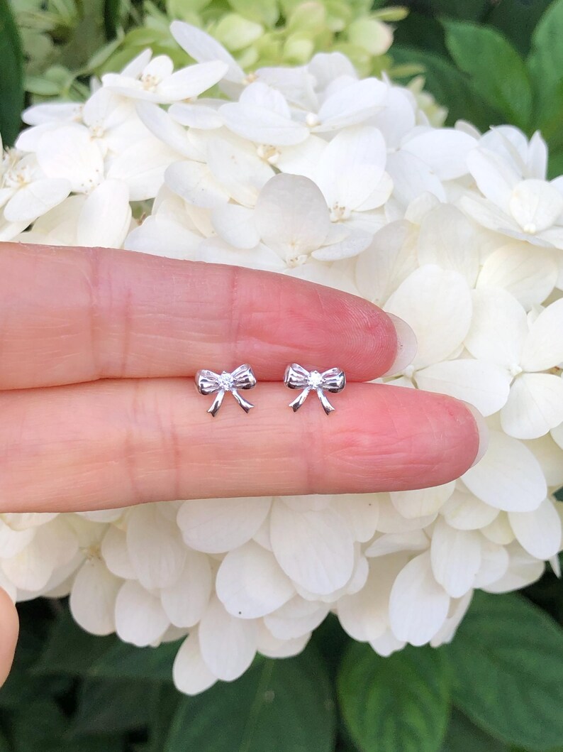May include: A pair of silver bow earrings with a small clear stone in the center of each bow.