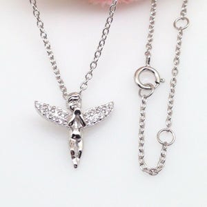 Puede incluir: Un collar de plata con un peque&ntilde;o colgante de &aacute;ngel. El &aacute;ngel tiene las manos juntas en oraci&oacute;n y tiene un peque&ntilde;o halo. El collar est&aacute; sobre un fondo blanco.