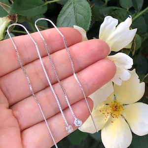 May include: Three silver chain earrings with a small clear crystal at the end of each chain.
