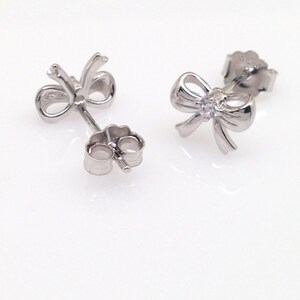 May include: A pair of silver bow earrings with a small clear stone in the center of each bow.