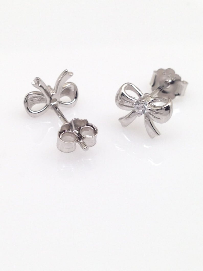 May include: A pair of silver bow earrings with a small clear stone in the center of each bow.
