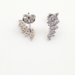 May include: A pair of silver earrings with a leaf design. Each earring has a row of small, clear stones that form the shape of a leaf.