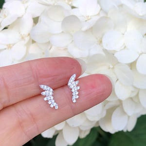 May include: A pair of silver earrings with a delicate, curved design. Each earring features a row of small, sparkling cubic zirconia stones.