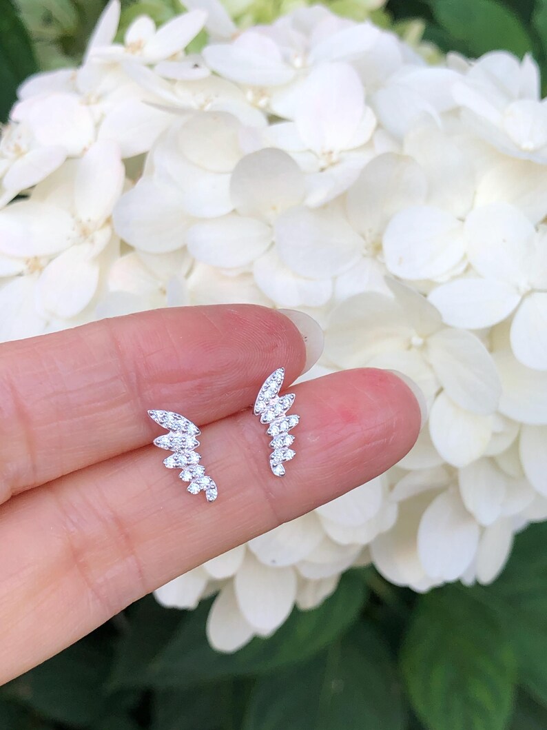 May include: A pair of silver earrings with a delicate, curved design. Each earring features a row of small, sparkling cubic zirconia stones.