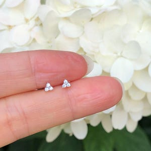 May include: A pair of silver stud earrings with three small, clear cubic zirconia stones arranged in a triangle shape.