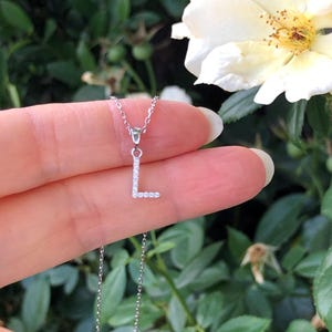 May include: A silver chain necklace with a small letter L pendant encrusted with tiny clear stones.