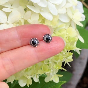May include: A pair of silver stud earrings with black gemstone accents. The earrings are small and delicate, and they would make a great gift for a friend or loved one.