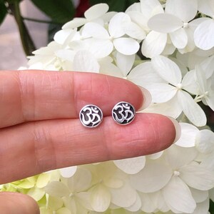 May include: A pair of silver Om symbol stud earrings. The earrings are small and round, with the Om symbol in the center.