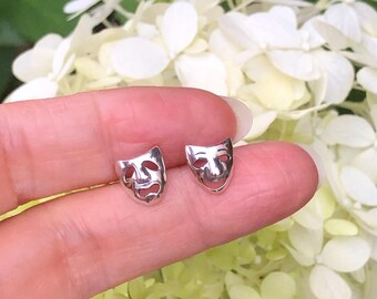 May include: A pair of silver earrings featuring a classic theater mask design. One mask is smiling, the other is frowning.